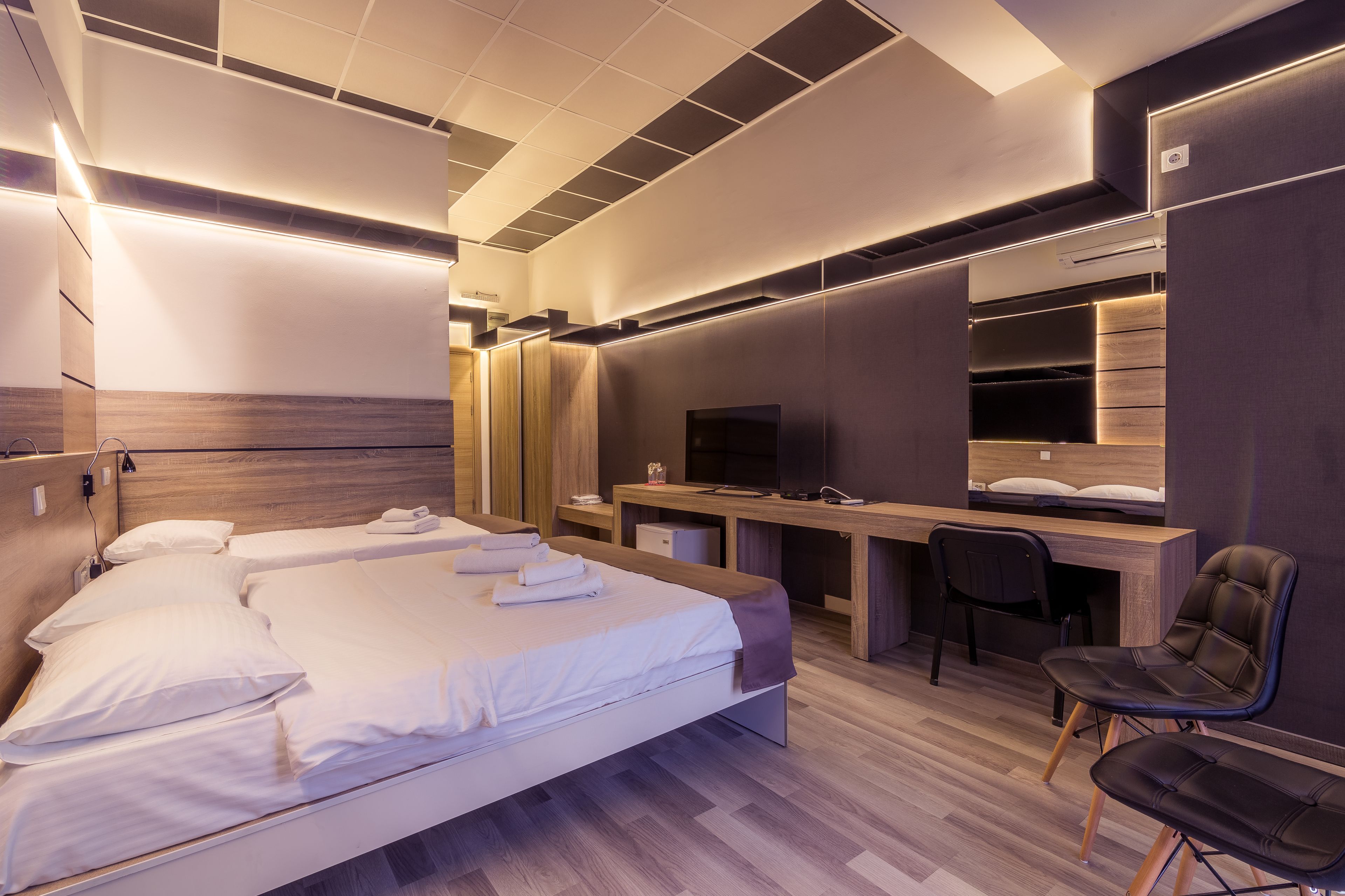 A modern hotel room with a bed, desk, chair, and built-in wardrobe.