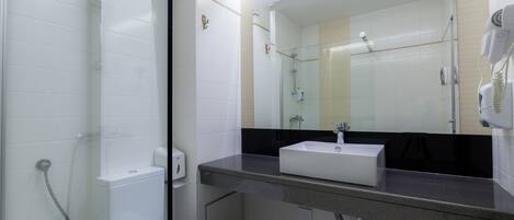 A bathroom with a toilet, sink, mirror, and shower.