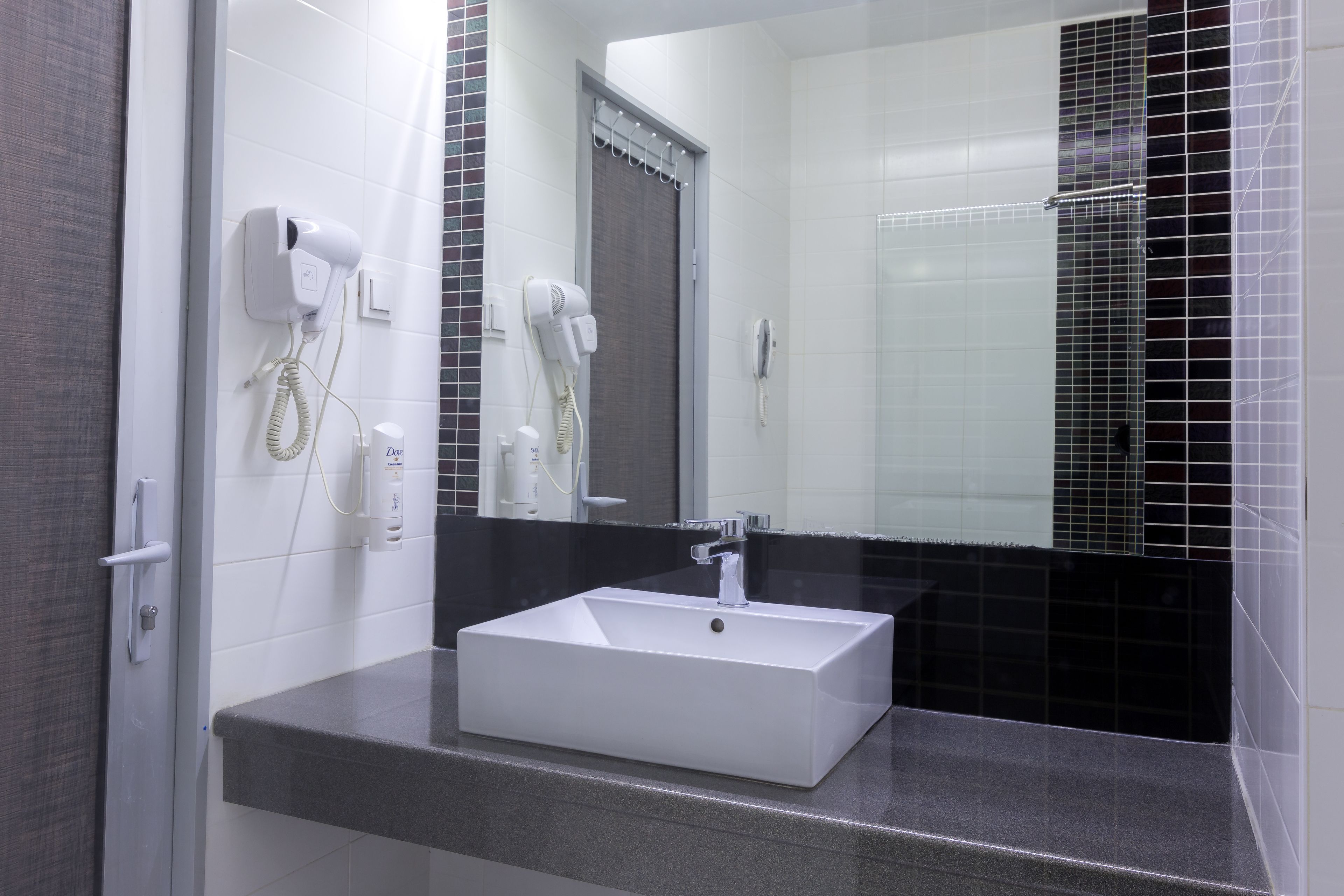A modern bathroom with a white sink, a mirror, and two hair dryers mounted on the wall.