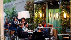 An outdoor café with tables and chairs, surrounded by greenery and decorative lighting.