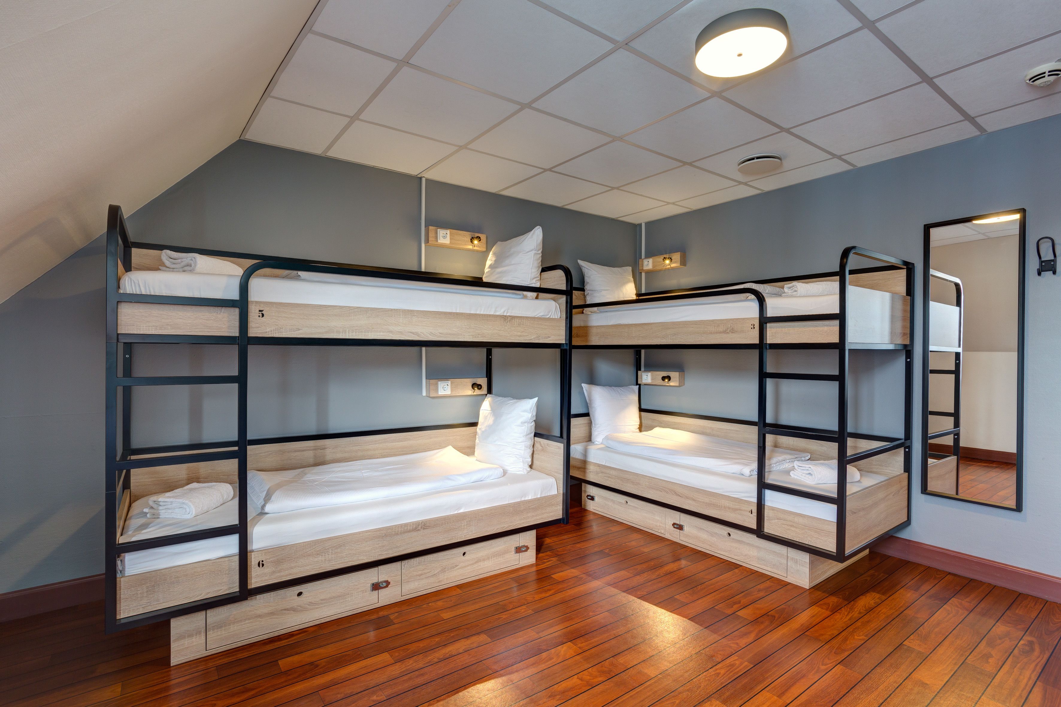 Ein Schlafsaalzimmer mit Stockbetten, Holzboden und einer Deckenleuchte.