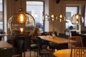 Een restaurantinterieur met ronde tafels en stoelen, hangende吊灯 en zicht op de straat.