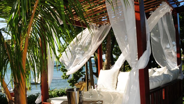 A beachside gazebo with a canopy, a wooden table with a champagne bucket and glasses, and a cushioned seating area. - Pousada Casa Búzios (Búzios)