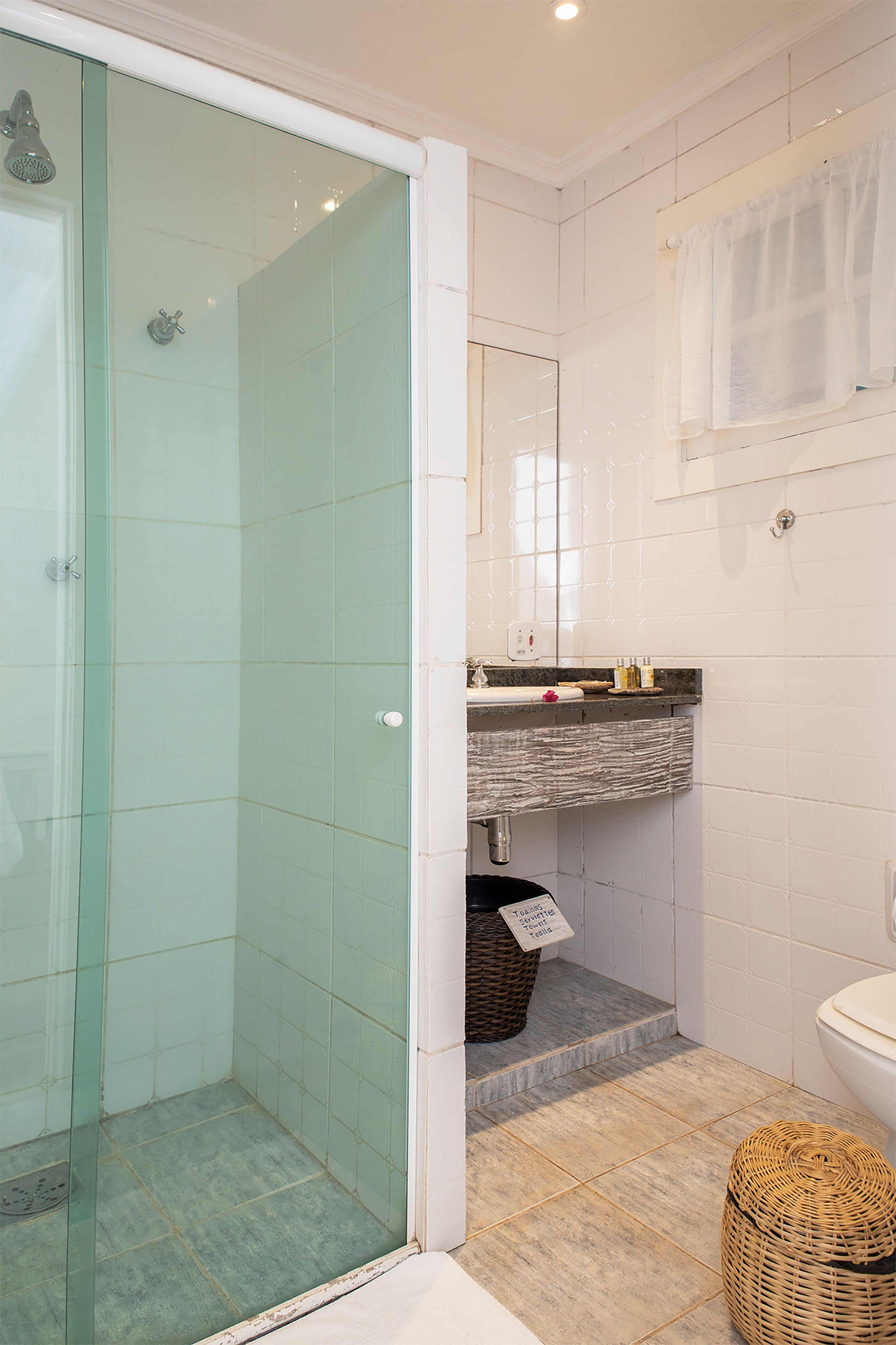 A bathroom with a glass shower enclosure, a sink with a marble countertop, and a toilet.