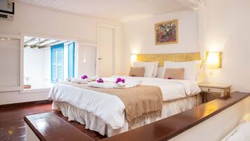 A well-lit bedroom with a large bed, a bedside table, and a window with blue shutters.