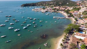 An aerial view of a coastal town with numerous boats docked at the marina, a sandy beach, and residential buildings. - Pousada Casa Búzios (Búzios)