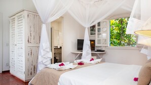 A bedroom with a canopy bed, a wardrobe, a television, and a window with a view of greenery. - Pousada Casa Búzios (Búzios)