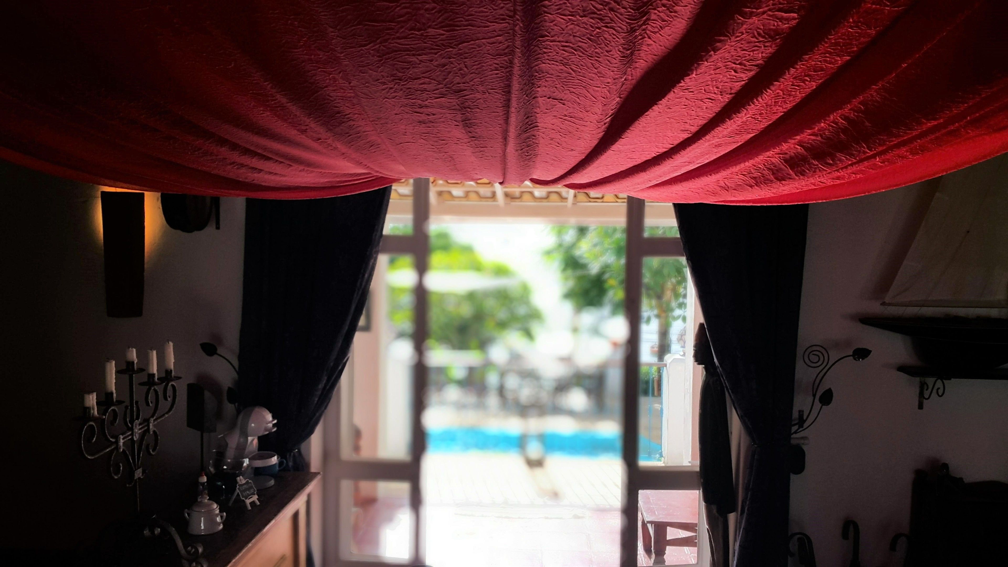 A room with a view of an outdoor pool, a bar area with a coffee machine, and a window with curtains.