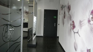 A hallway with a black door, a glass wall with a Wi-Fi sign, and a wall with floral artwork. - Albergo Renato (Sesto San Giovanni)