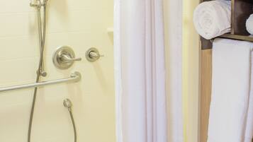 A shower with a handheld showerhead, a glass-enclosed tub, and a towel rack with folded towels.