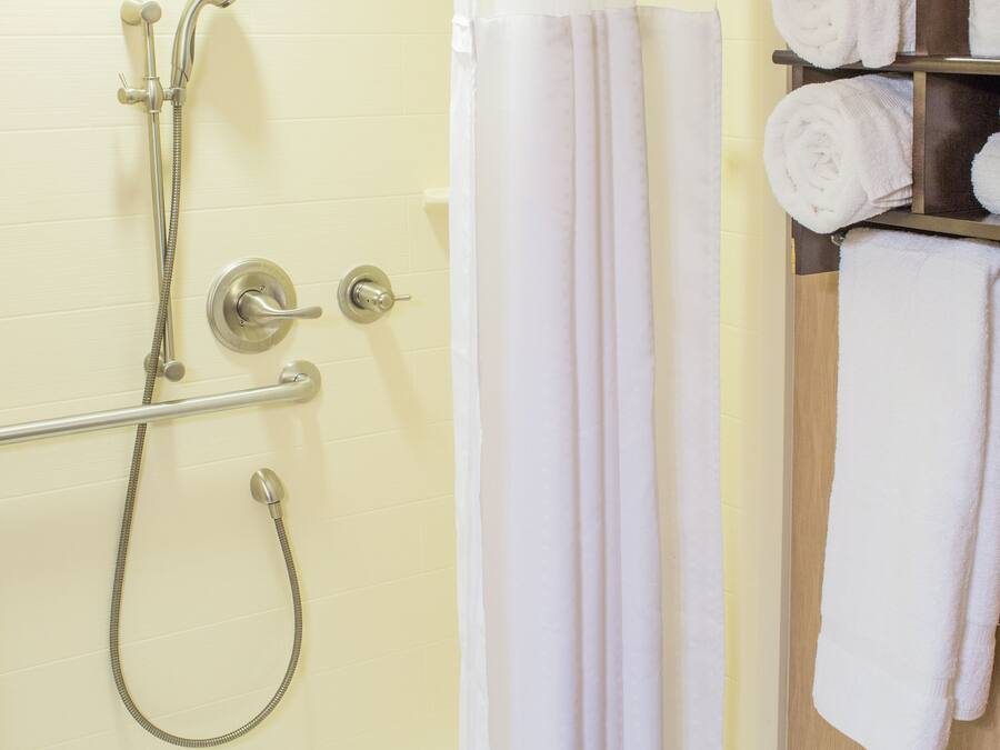 A shower with a handheld showerhead, a glass-enclosed tub, and a towel rack with folded towels.