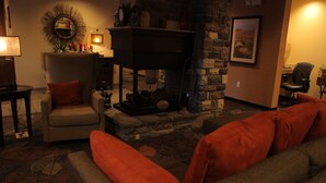 A cozy living room with a fireplace, a comfortable armchair, and a sofa. - Little Missouri Inn & Suites (Watford City)