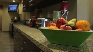 A kitchen counter with a green bowl containing fruits and a red container in the background. - Little Missouri Inn & Suites (Watford City)