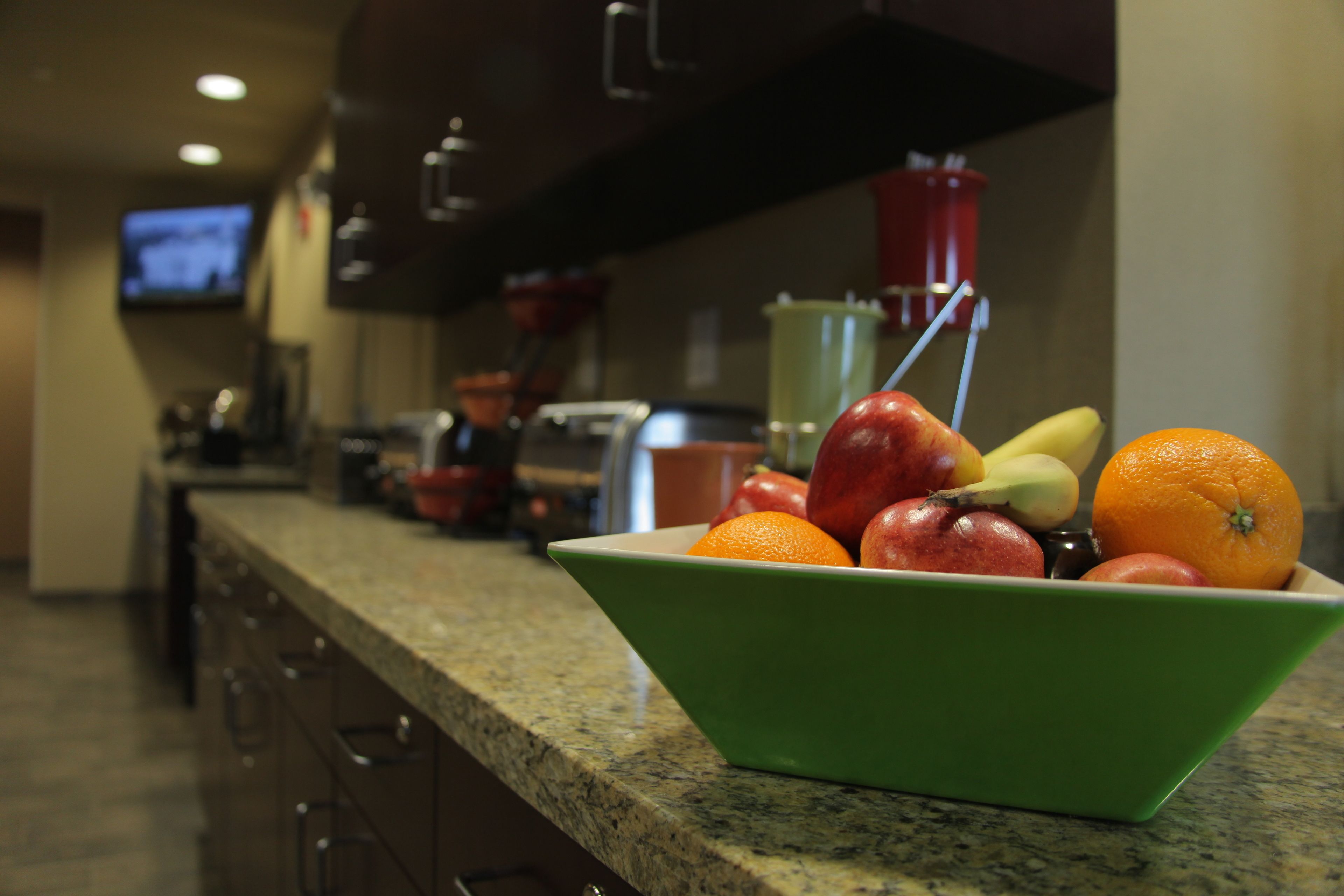 Una encimera de cocina con un tazón verde que contiene frutas y un recipiente rojo al fondo.