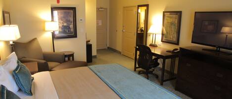 Una habitación de hotel con cama, escritorio, silla, televisor y cómoda.