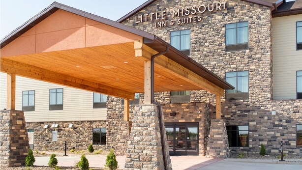 Ein Hotel mit einer Stein-Fassade, einem überdachten Eingang und einem Schild mit der Aufschrift 'Little Missouri Inn & Suites'.