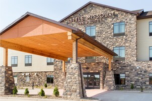 Un hotel con fachada de piedra, un acceso cubierto y un letrero que dice "Little Missouri Inn & Suites".