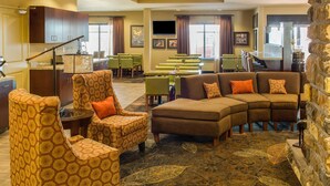 Eine Hotelhalle mit Ecksofa, gemusterten Sessel, Essbereich und einer Wand aus Stein.