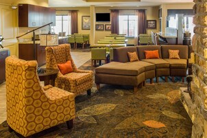 Un hall de hotel con un sofá modular, sillones estampados, una zona de comedor y una pared de acento de piedra.