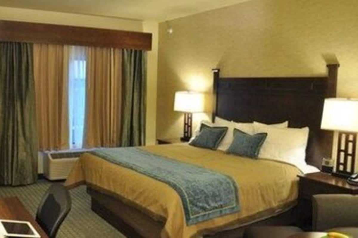 Une chambre d’hôtel comprenant un lit, deux lampes de chevet, une télévision, un bureau avec une chaise et une fenêtre avec des rideaux.