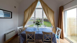 A dining area with a table set for two, a window with curtains, and a view of the outdoors.