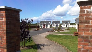 A residential street with brick houses, a paved driveway, and a grassy area.