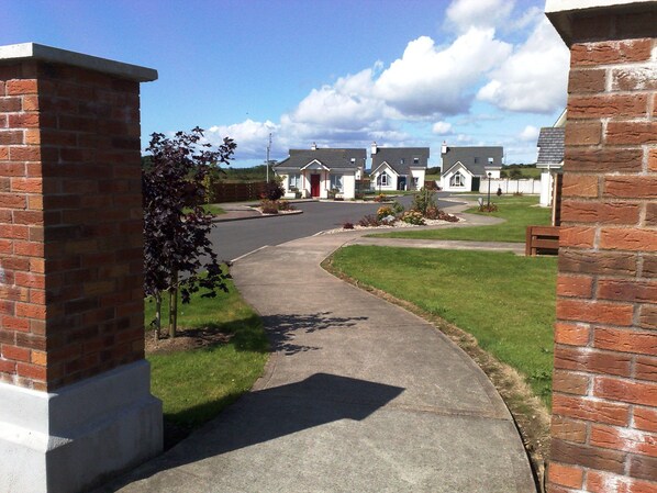 A residential street with brick houses, a paved driveway, and a grassy area.