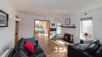 A modern living room with a fireplace, black leather sofas, a wooden coffee table, and a television.