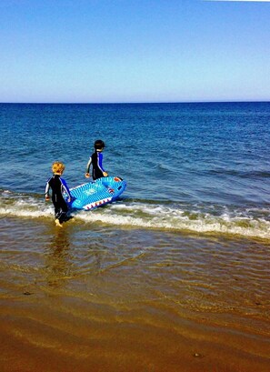 A beach scene with two people carrying a blue inflatable surfboard.