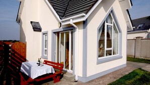 A house with a white exterior, a red bench, and a table with a bottle.