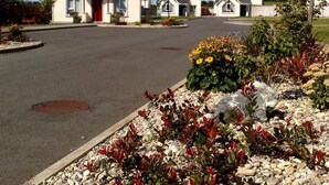 A row of single-story houses with a paved driveway and a landscaped garden area with various plants and flowers.