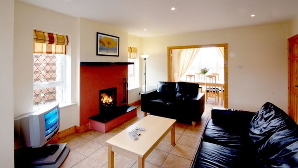 A living room with a fireplace, black leather sofa, and a television.