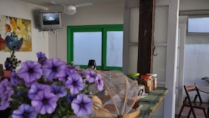 A kitchen with a green door, a television mounted on the wall, and a table with jars and a basket. - Pousada Casa das Rosas (Búzios)