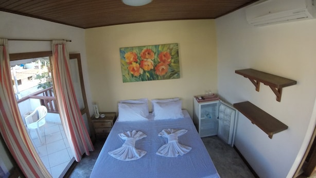 A room with a bed, a painting of flowers, a small table, and a shelf. - Pousada Casa das Rosas (Búzios)