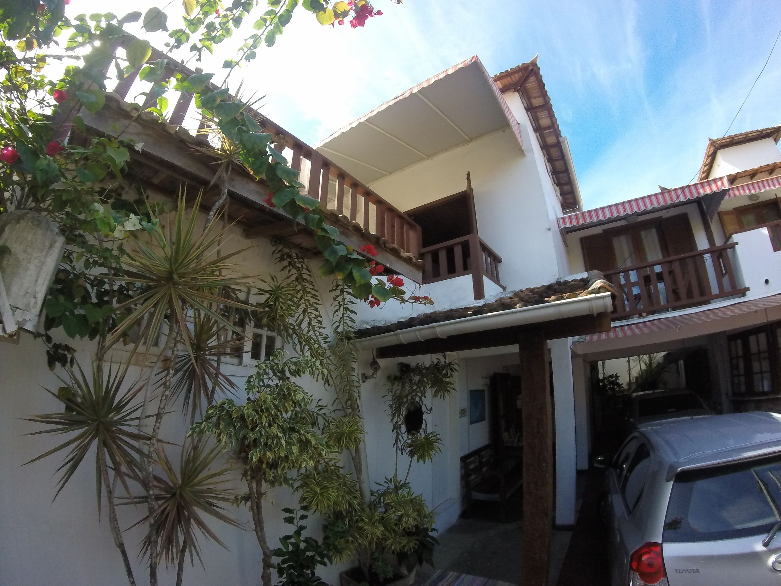 A two-story building with a balcony, potted plants, and a parked car.