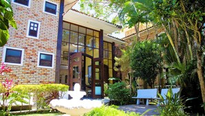 A building with a brick facade, large windows, and a garden with a fountain and seating area. - Pousada Casa da Praia (Búzios)