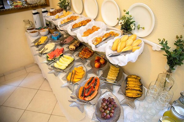 A buffet table with various fruits, cheeses, and bread. - Pousada Casa da Praia (Búzios)