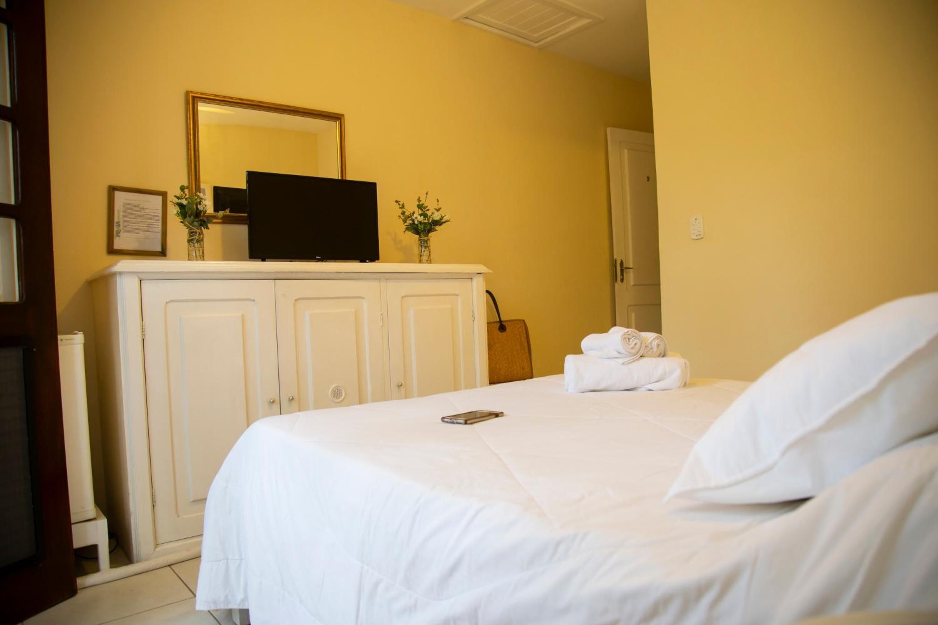 Una habitación de hotel con una cama, un televisor sobre un mueble y un espejo en la pared.