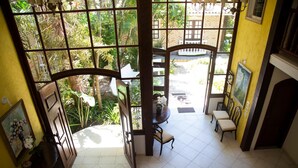 A room with a view of a garden through large windows, a dining area with chairs and a table, and a staircase leading to an upper level. - Pousada Casa da Praia (Búzios)
