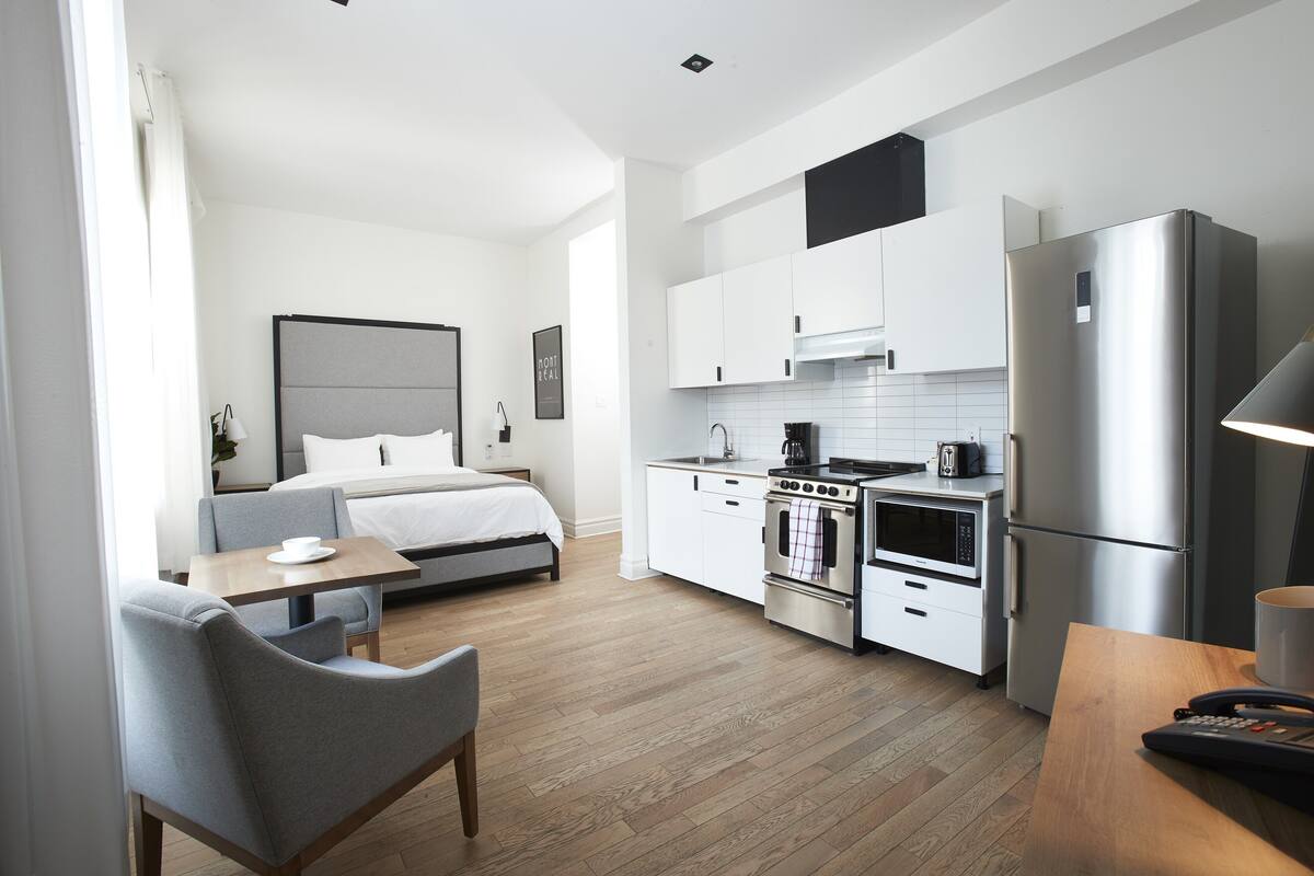 Ein modernes Hotelzimmer mit Bett, einer kleinen Essecke, einer Küchenzeile und einem Badezimmer.
