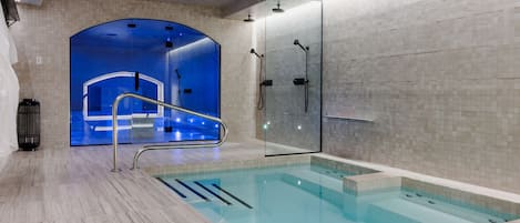 A modern indoor pool area with a glass-enclosed shower, a clear pool, and a tiled floor.