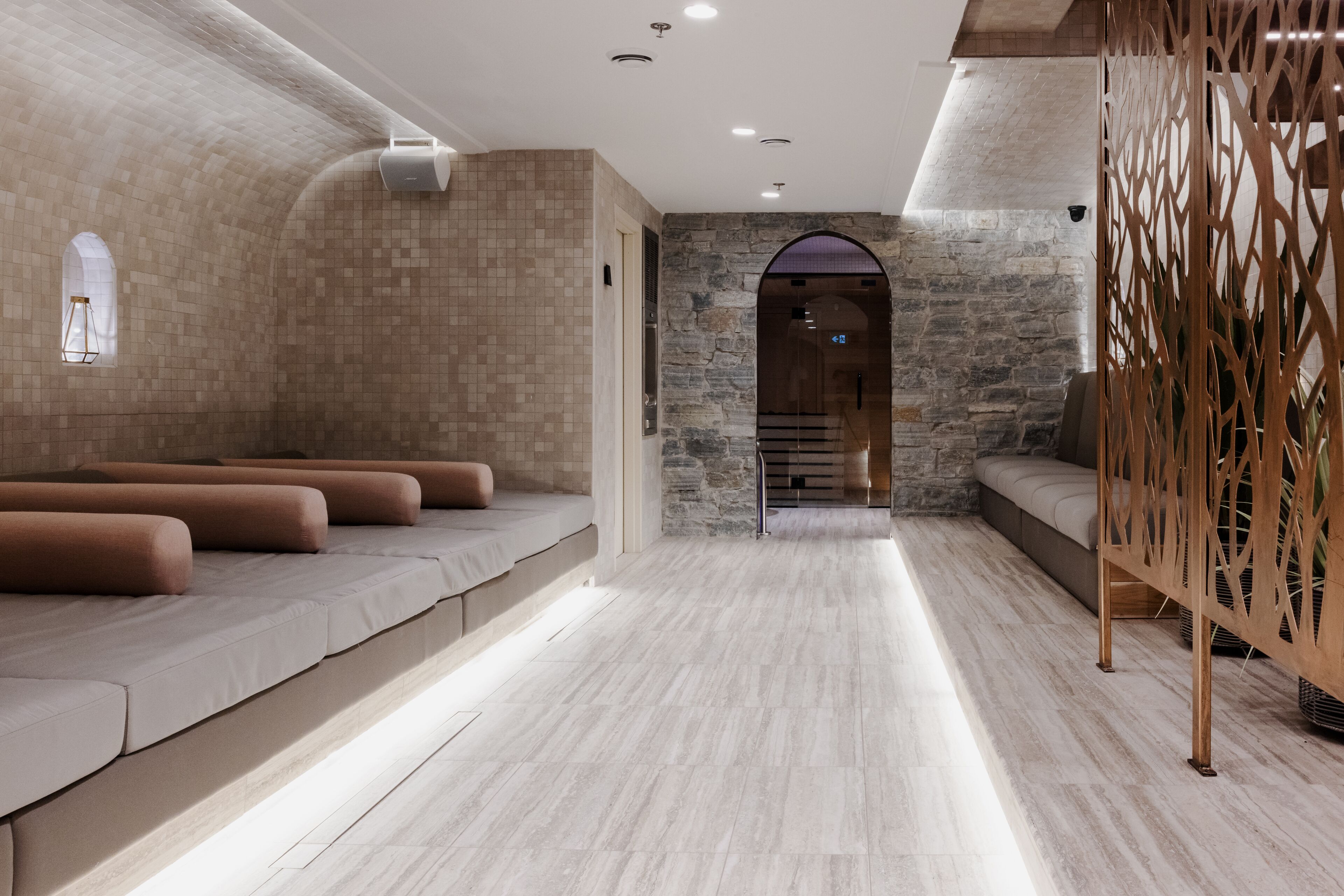 A spa area with a stone wall, a wooden partition, and a seating area with cushions.