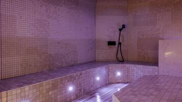 A bathroom with a tiled floor and walls, a shower area with a handheld showerhead, and a bench.