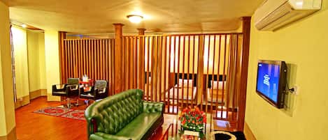 A living room with a green sofa, a coffee table with a magazine, and a TV on the wall.