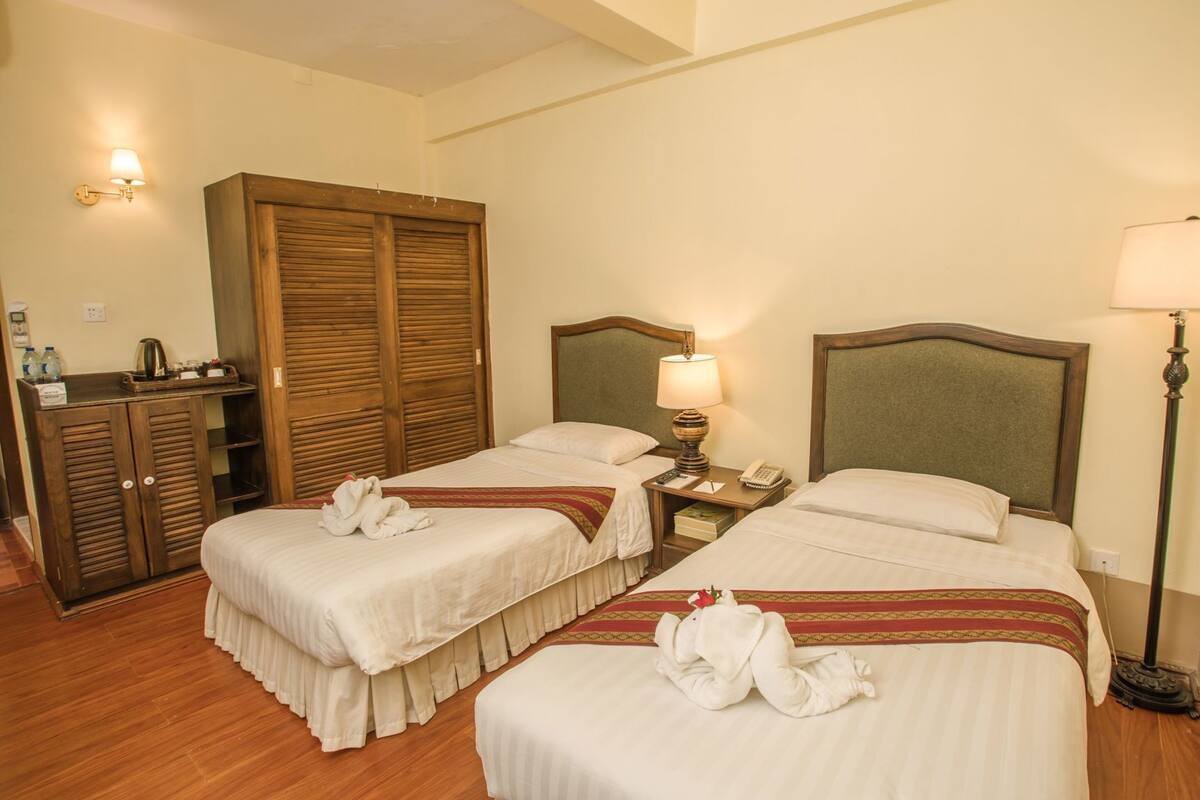 A hotel room with two beds, wooden wardrobe, bedside lamps, and a small table with a telephone.