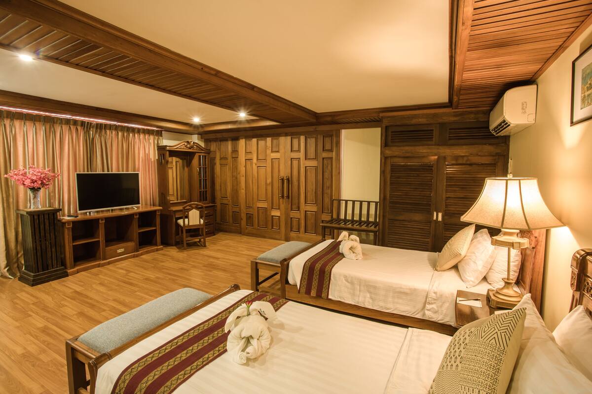 A hotel room with two beds, a TV, wooden furniture, and a lamp.