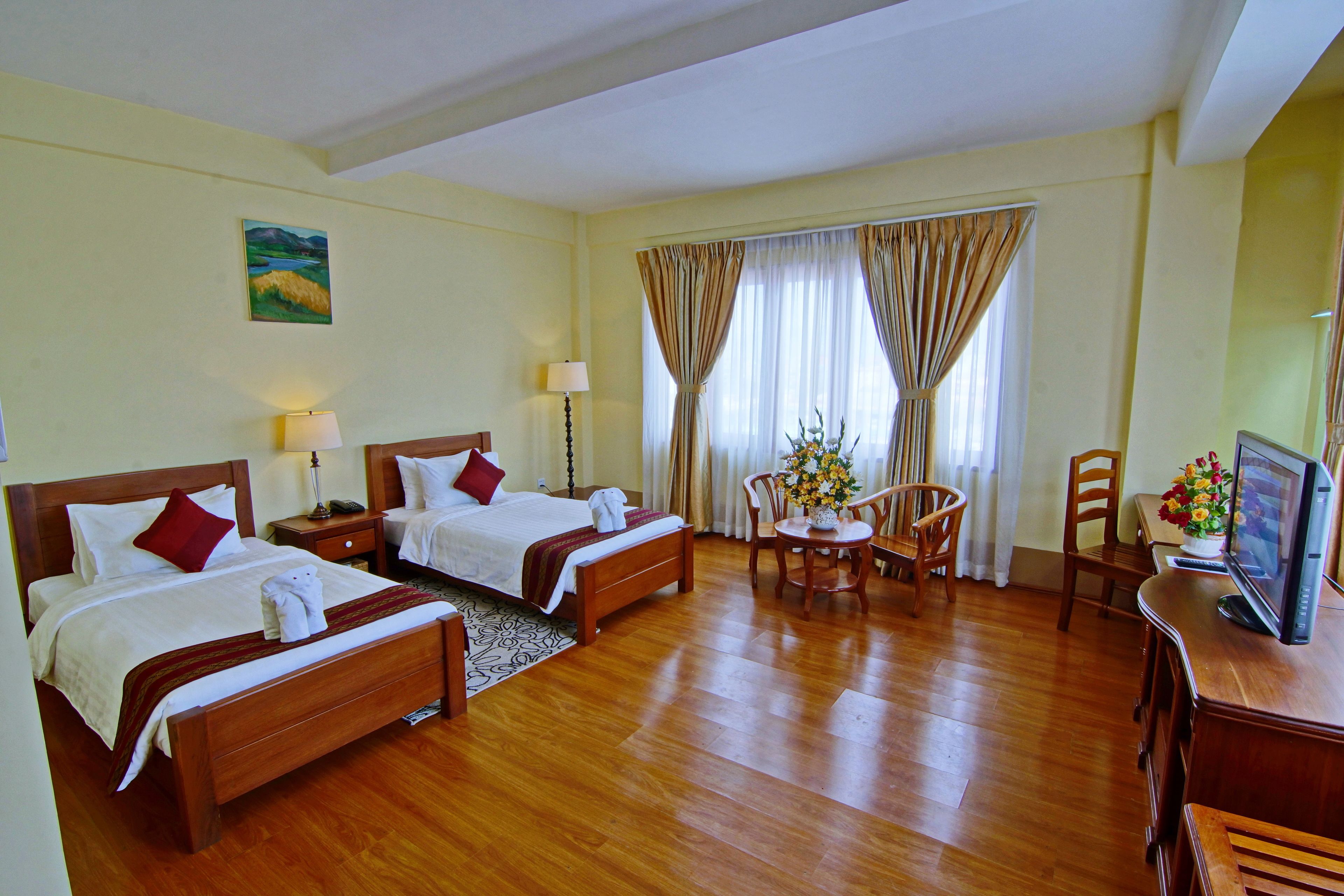 Habitación de hotel con dos camas, un escritorio, una silla, un televisor y una ventana con cortinas.