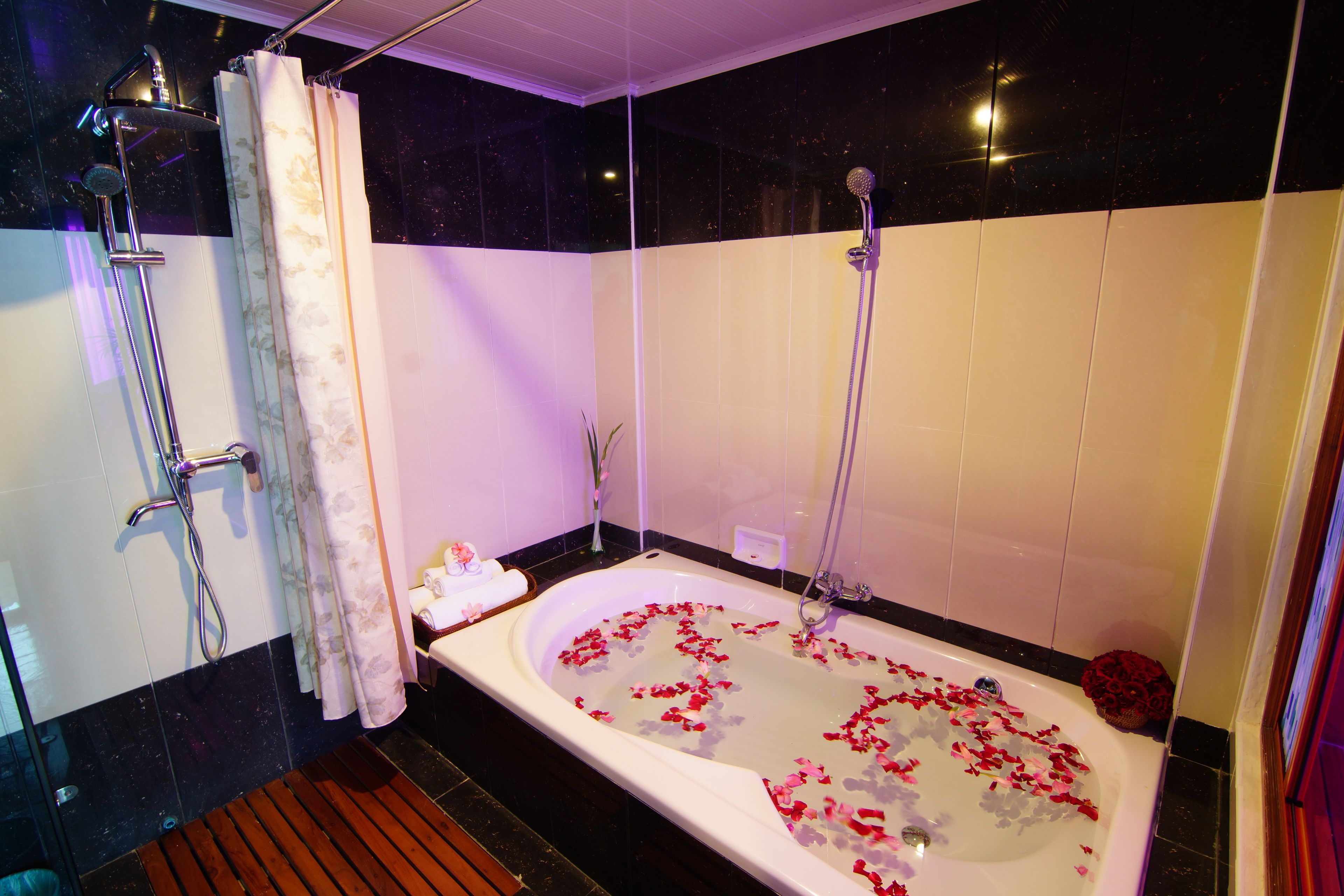 Un baño con una bañera llena de pétalos de rosa, una zona de ducha y un tapete de baño de madera.