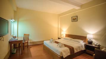 Ein Hotelzimmer mit Bett, Nachttischlampen, einem Schreibtisch mit Stuhl, einem Fernseher und einem gerahmten Bild an der Wand.