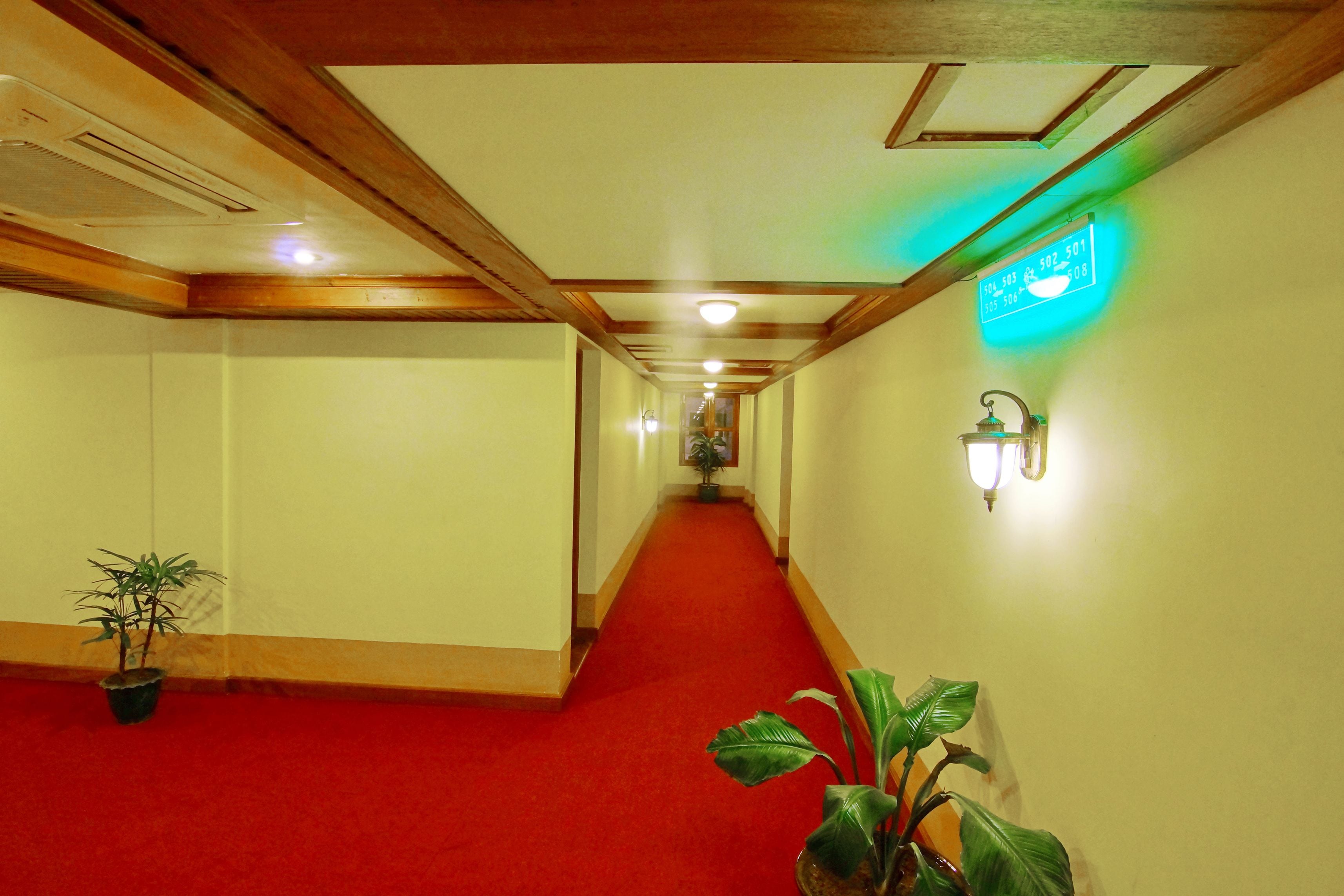 A hotel hallway with a red carpet, wooden ceiling beams, and wall-mounted light fixtures.